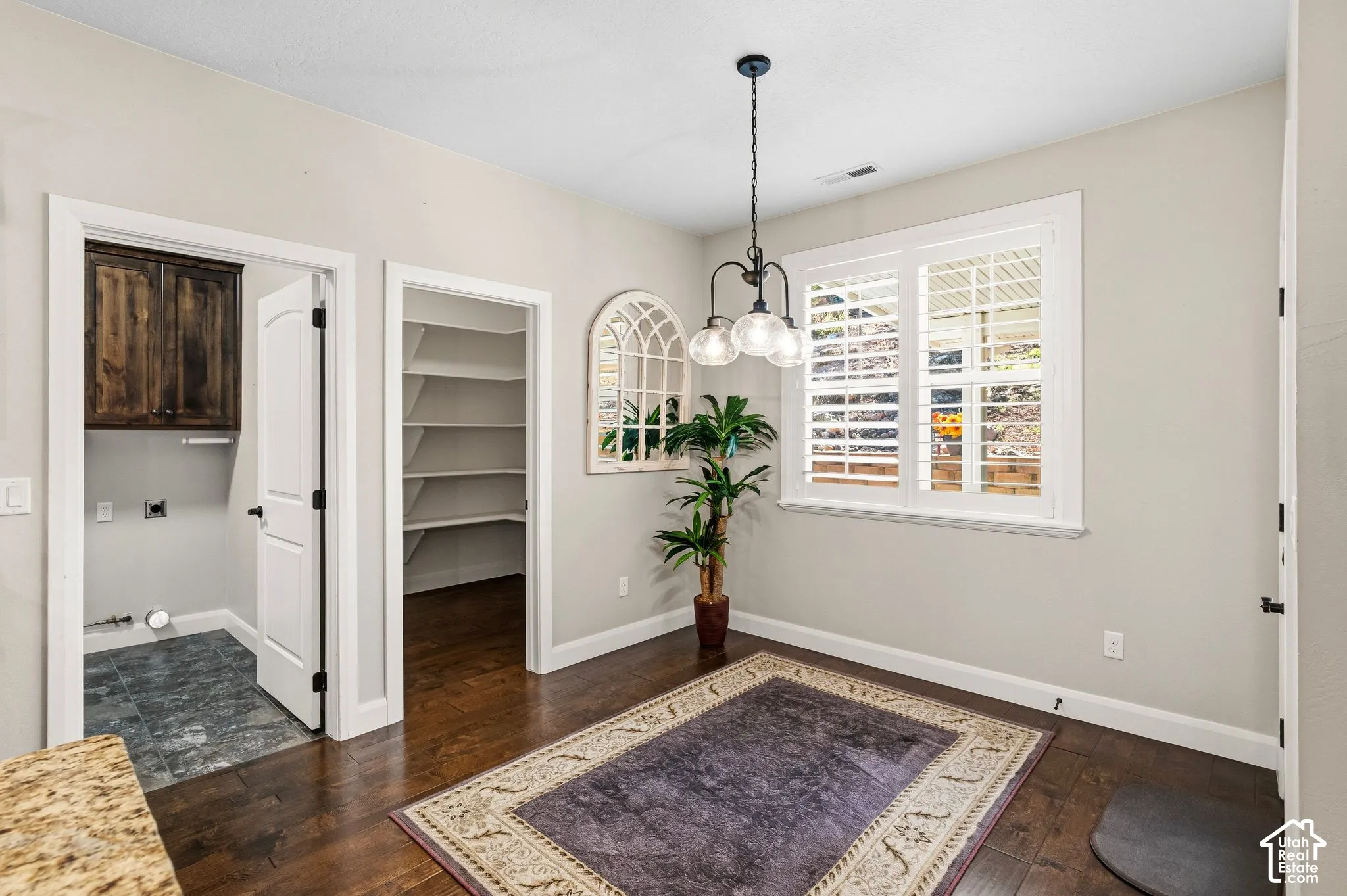 Wood-finish flooring, white plantation shutters, built-in pantry shelving, and a laundry area with dark wood-finish cabinetry