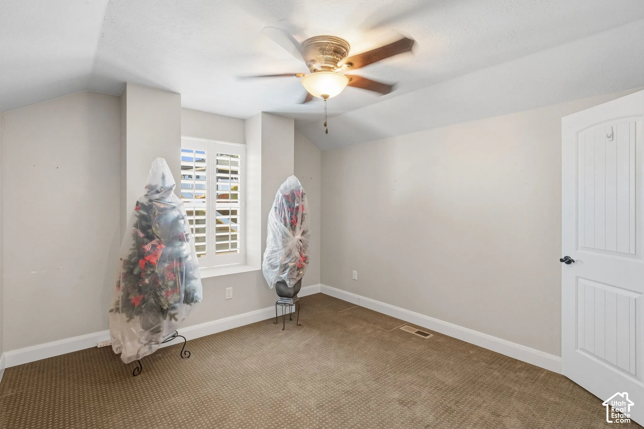 Ceiling fan with integrated lighting, wall-to-wall carpeting, window with plantation shutters, white paneled door, and neutral wall finishes