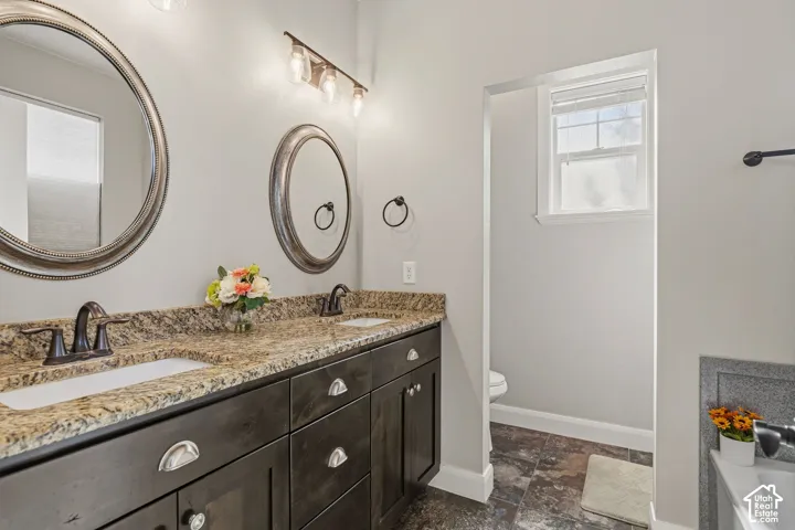 Dual vanity with integrated sinks, granite-style countertop, dark wood-finish cabinetry, and framed mirrors