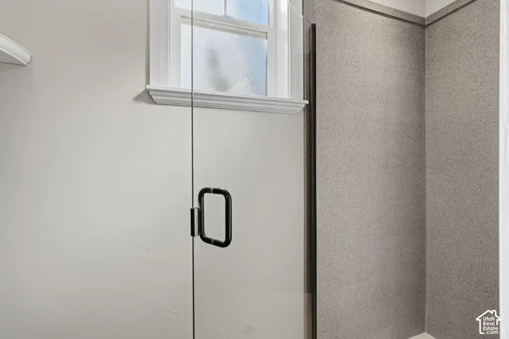 Frameless glass shower enclosure with a matte black handle and textured wall panels