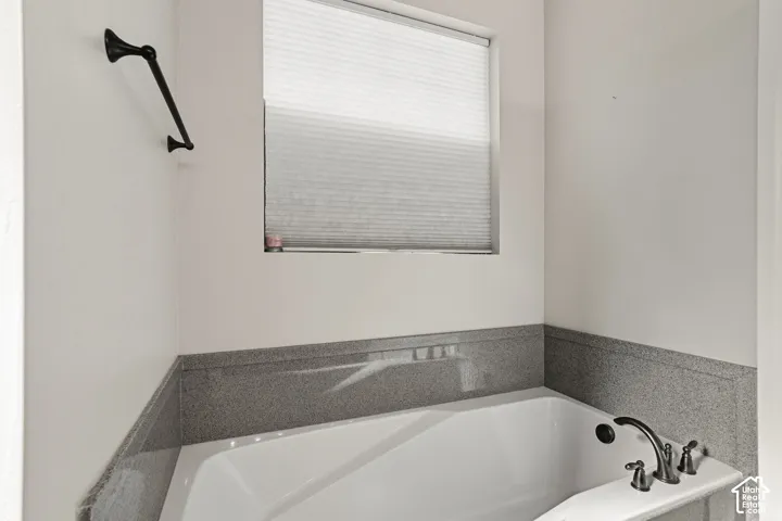 White soaking tub with dark bronze fixtures and a surrounding gray stone-look finish
