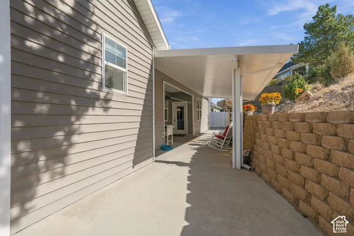 Covered concrete patio with a retaining wall, tan horizontal siding, and a white framed window