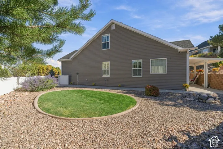 Exterior siding, multiple windows with white frames, covered patio structure, gravel landscaping, and a circular lawn feature