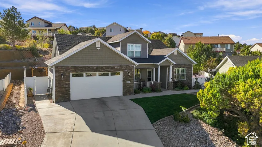 Stone and siding exterior with an attached garage, covered entry, and a sloped, landscaped lot featuring a manicured lawn