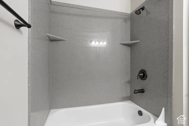 Bathtub with textured wall surround, matte black shower fixtures, and built-in corner shelving