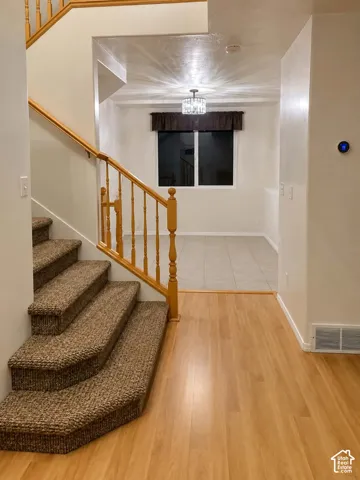 Wood-finish flooring, carpeted staircase, wood banister and balusters, and a contemporary ceiling light fixture