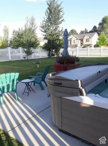 Expansive backyard featuring a hot tub, concrete patio, and white picket fencing