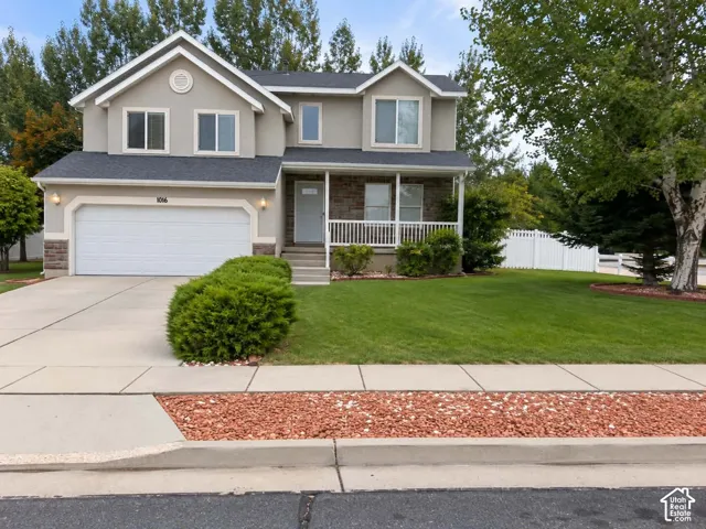 Two-story stucco exterior with stone accents, attached two-car garage, covered porch with white railings, and a fenced backyard