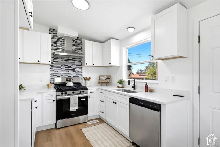 Modern kitchen featuring white cabinetry, stainless steel appliances including a gas range and dishwasher, quartz countertops, mosaic tile backsplash, and a large window with natural light