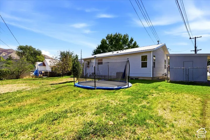 Spacious backyard with mature landscaping and lush lawn, featuring a trampoline and detached storage structure