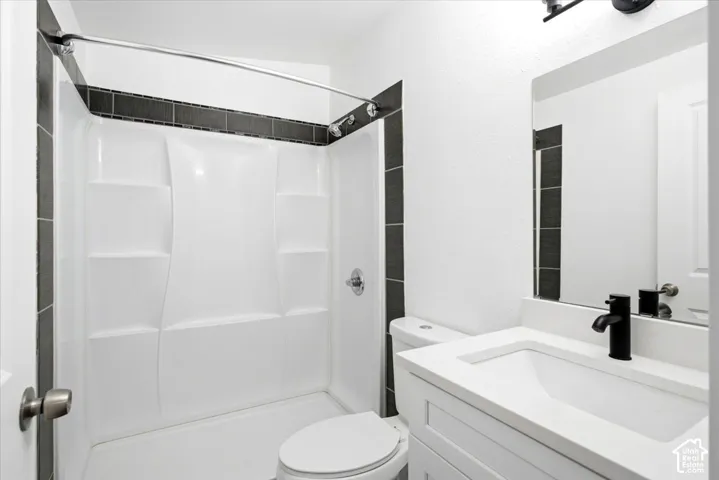 Bathroom featuring a white shower surround, dark tile accent, white vanity with integrated sink, and matte black fixtures