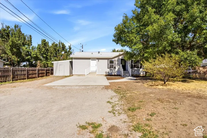 Light-toned exterior with a metal roof, featuring a concrete patio and a detached storage shed