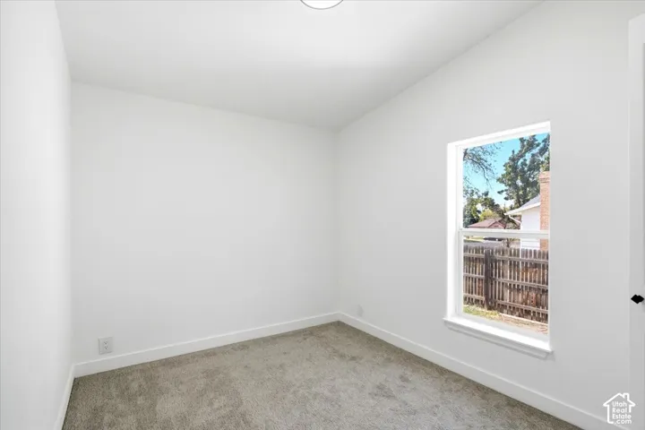 Vaulted ceiling, neutral wall tones, gray carpet, single window, and a flush mount ceiling light