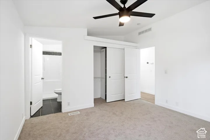 Neutral colored carpeted flooring, white walls, and a dark-toned ceiling fan with integrated lighting