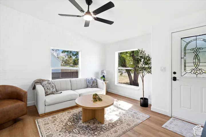 Vaulted ceiling, wood-finish flooring, white walls, black ceiling fan with integrated lighting, and a front entry door with decorative glass