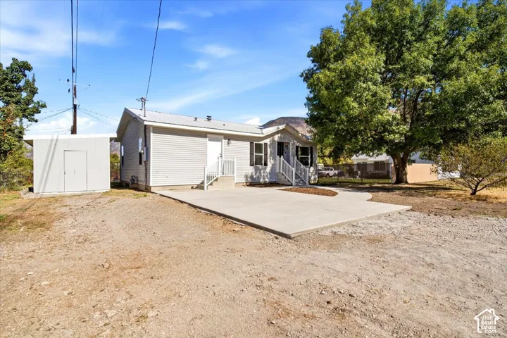 Exterior featuring light-colored siding, a metal roof, a concrete patio, a detached storage shed, and mature trees