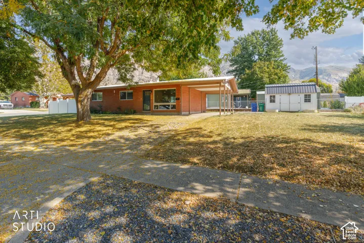 Brick exterior, large mature tree, expansive front lawn, paved driveway, detached storage shed, mountain backdrop