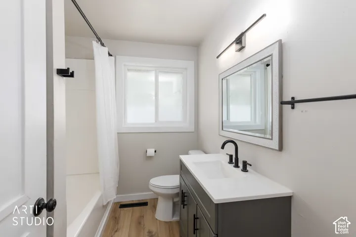 Built-in vanity with a white countertop and matte black fixtures, framed mirror, window with white trim, and wood-finish flooring