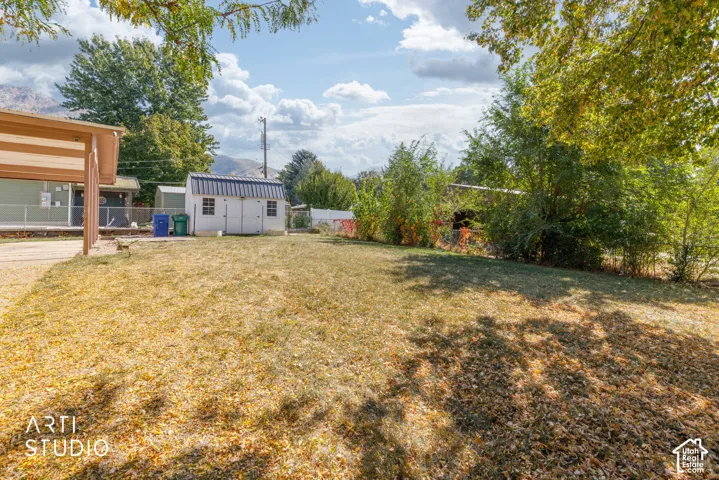 Expansive grassy area with a detached white storage shed featuring a dark metal roof