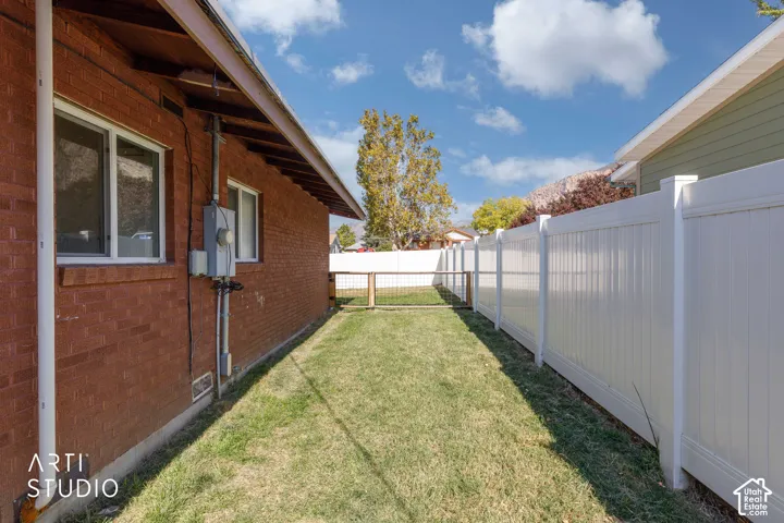 Brick exterior with white-framed windows, accompanied by a white privacy fence and a grassy side yard