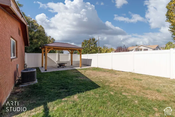 Fenced backyard featuring a wood gazebo with a metal roof, a concrete patio, and a grass lawn