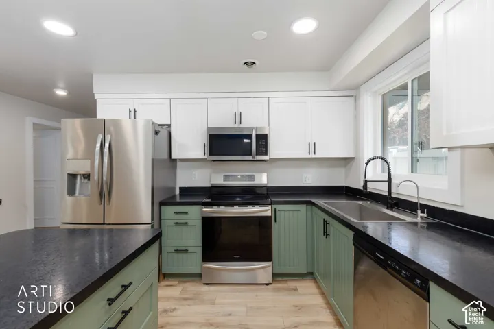 Kitchen featuring white upper cabinetry, green lower cabinetry, stainless steel appliances, dark countertops, and wood-finish flooring