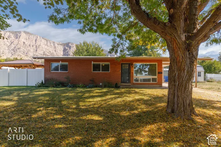 Brick exterior with a large picture window, carport, and mature front yard tree