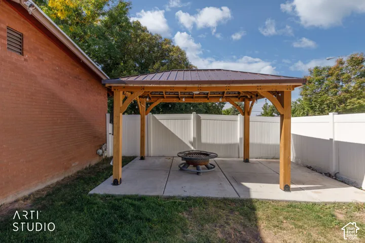 Outdoor wooden pergola with a metal roof, concrete patio, and white privacy fencing