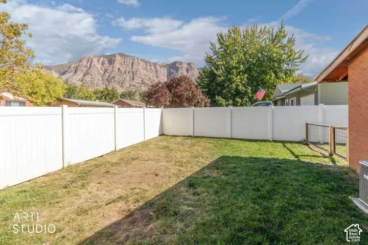 Expansive backyard featuring a white privacy fence, mature trees, and a mountain backdrop