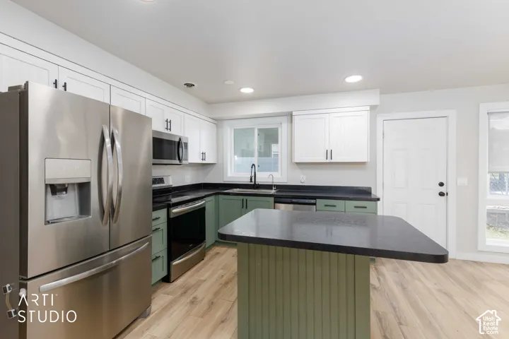 Kitchen featuring two-tone cabinetry, stainless steel appliances, dark countertops, a central island, and wood-finish flooring