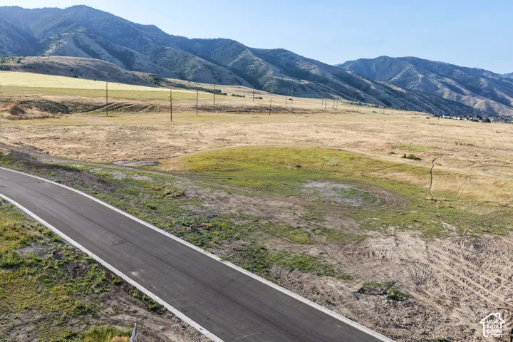 Expansive undeveloped land parcel featuring paved road frontage, natural topography, and a backdrop of mountain terrain