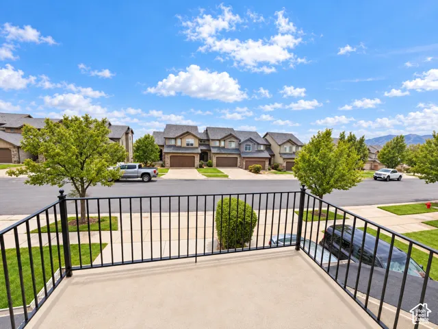 Balcony with black metal railing, overlooking a street with mature trees and residential properties