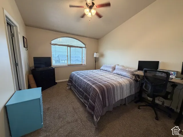 Carpeted room featuring a ceiling fan, sloped ceiling, and an arched window