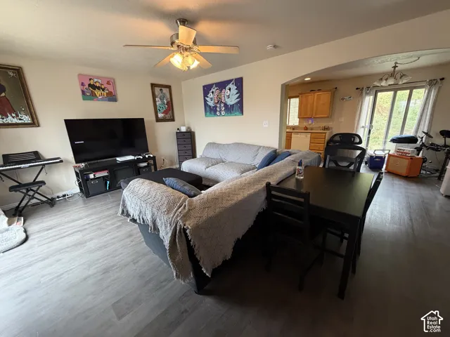 Wood-finish flooring throughout, ceiling fan with integrated lighting, and an arched doorway leading to a kitchen with wood cabinetry