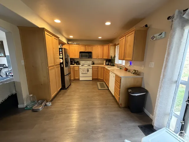 Galley kitchen featuring wood-finish flooring, wood cabinetry, recessed lighting, and a white appliance package