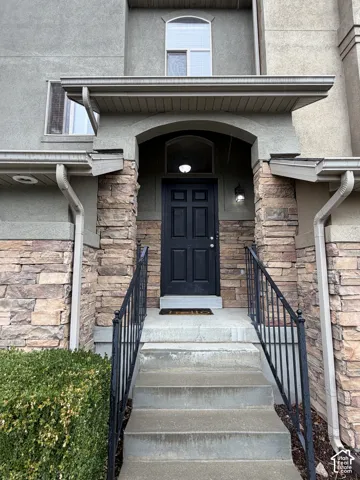 Stucco exterior with stone accents, featuring a black paneled entry door, arched entryway, and concrete steps with black metal railings