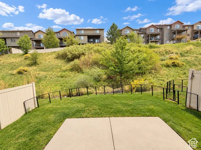 Expansive lawn featuring a concrete patio, a partial vinyl fence, and a black metal fence