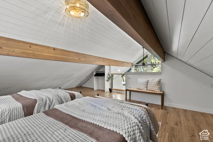 Vaulted ceiling with exposed wood beams, wood-finish flooring, and a built-in closet