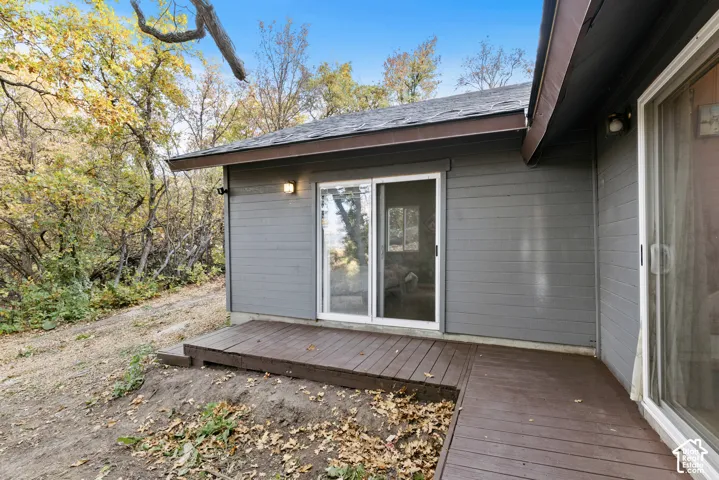 Exterior featuring horizontal siding, dark brown decking, white-framed sliding glass doors, and a partial roofline
