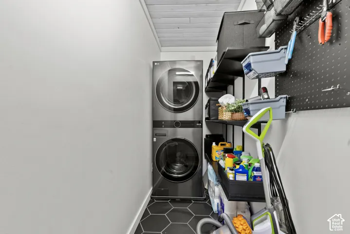 Stacked washer and dryer unit, hexagonal floor tiling, white wood-plank ceiling, black shelving, and black pegboard storage