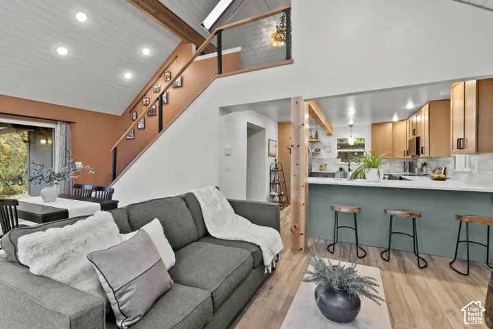 Open-concept living and kitchen space featuring a gray upholstered sofa, wood-finish flooring throughout, and a chef's kitchen with white cabinetry, quartz countertops, and seating at a waterfall-edge island