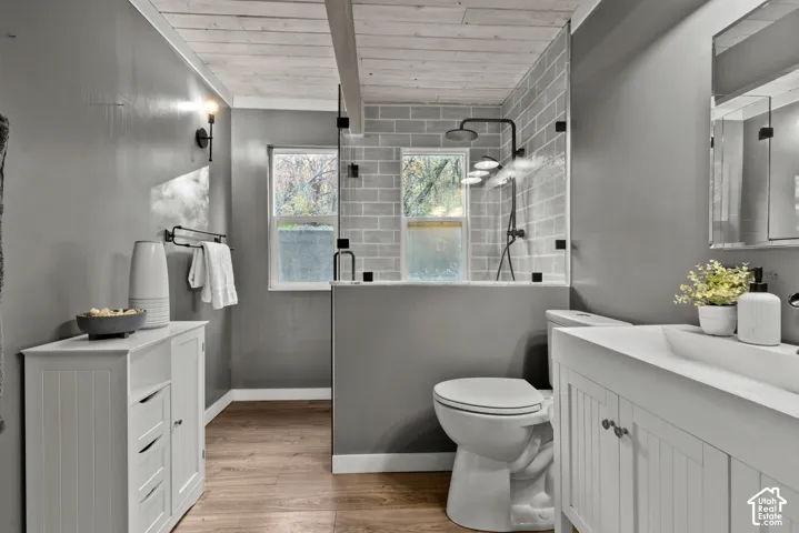 Bathroom featuring wood-finish flooring, a white vanity with a rectangular basin, a walk-in shower with subway tile, and a wood-paneled ceiling