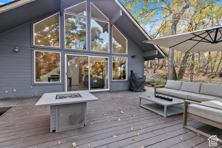 Expansive deck with wide plank flooring, a built-in fire feature, and sliding glass doors leading into the interior