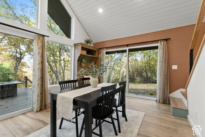 Vaulted ceiling with wood-finish planks, large glass panel windows, sliding glass door access to an exterior deck, wood-finish flooring, and built-in shelving with storage