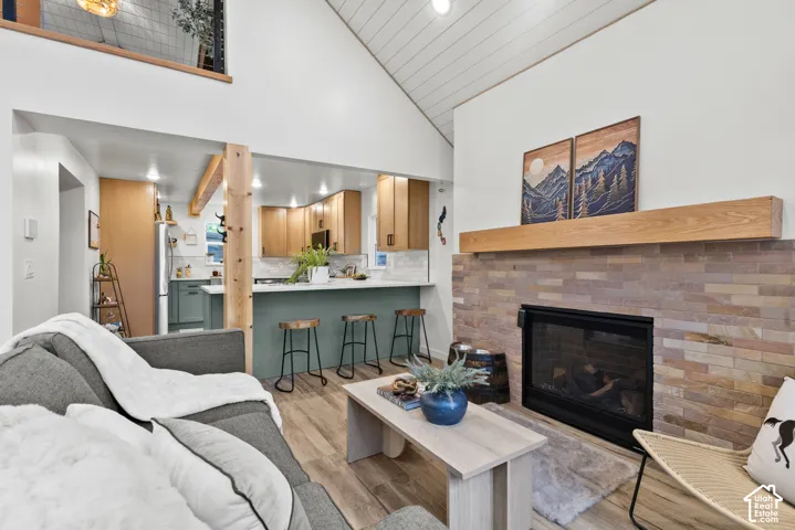 Vaulted ceilings, a stone-clad fireplace with a wood mantel, wood-finish flooring, and a kitchen featuring a peninsula with countertop seating