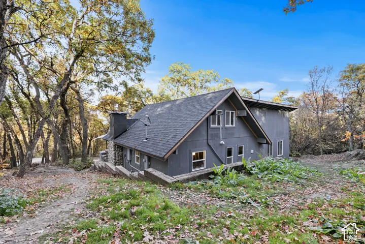 Contemporary exterior with dark siding, a dark shingle roof, multiple windows, and a stone chimney