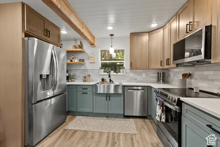 Kitchen featuring wood-finish flooring, two-tone cabinetry, stainless steel appliances, a farmhouse sink, and a tiled backsplash