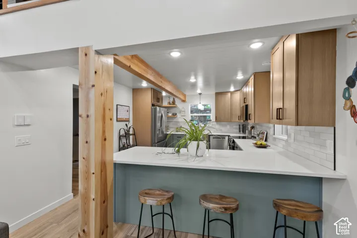 Kitchen featuring light wood-finish cabinetry, a white subway tile backsplash, recessed lighting, and a kitchen island with a light-colored countertop