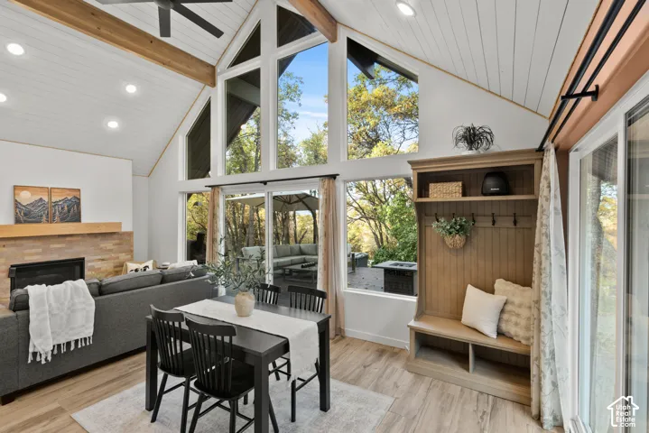 Vaulted ceilings with exposed wood beams, expansive floor-to-ceiling windows, wood-finish flooring, built-in fireplace with stone surround, and a built-in hall tree with bench seating