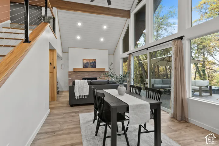 Vaulted ceiling with exposed beams, wood-finish flooring, floor-to-ceiling windows, brick fireplace surround with wood mantle, and a cable railing staircase